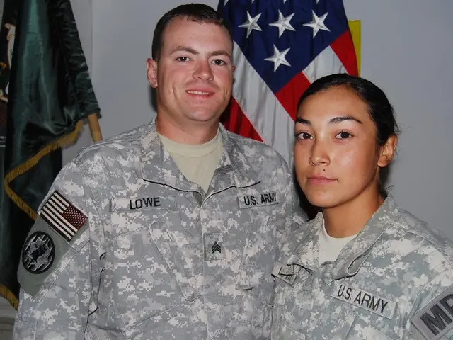 In this image there are two persons with uniform, behind them there are few flags and the wall.