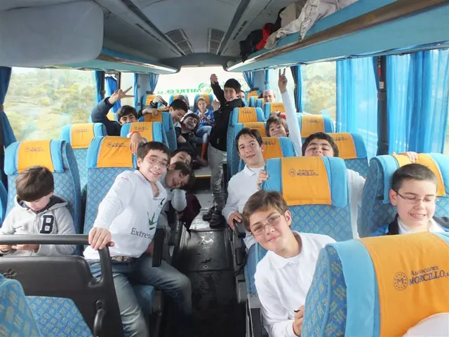 In this image there are group of persons sitting on a seat inside the bus. On the right side of the...
