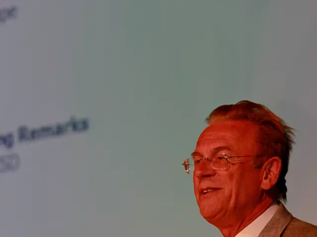 In this picture, we see a man in the white shirt and the grey blazer is standing. He is smiling and...