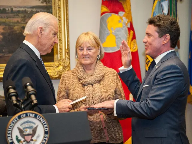 This image consists of three persons. The two men are wearing black suits. To the left, there is a...