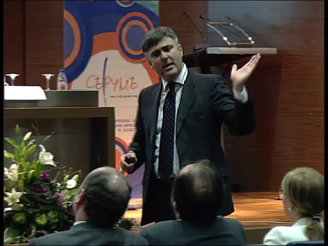 At the bottom of the picture, we see two men and a woman are sitting on the chairs. In front of...