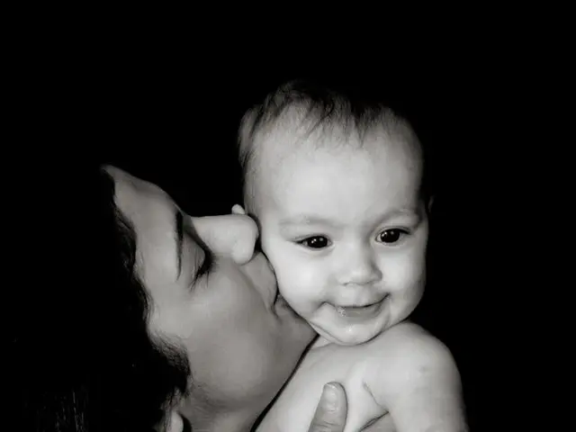 This is a black and white image. In this image we can see a woman holding and kissing the baby.