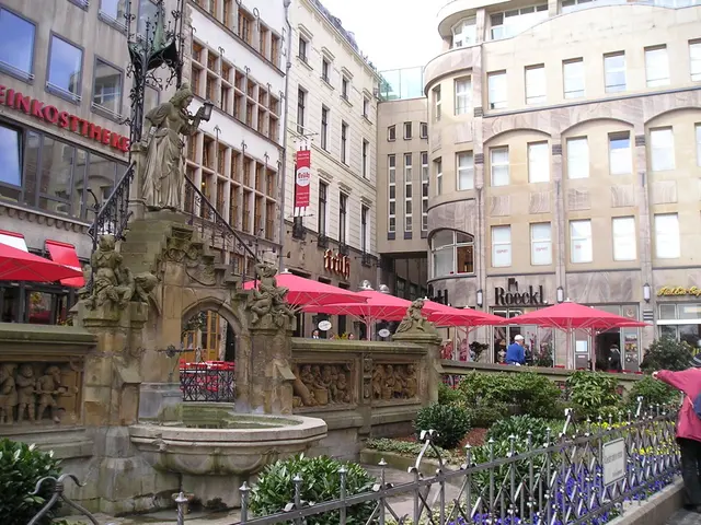 The picture is taken outside a city. In the foreground of the picture there are plants, railing,...