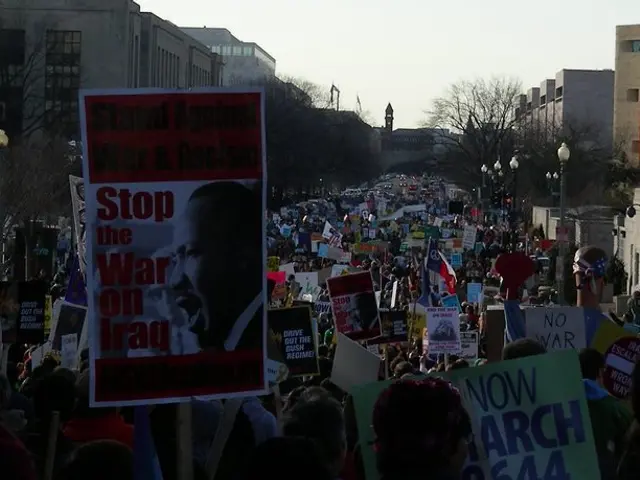 In this image there are people protesting on a road holding posters in their hands, in the...