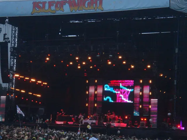 In this image we can see stage with lights. Also there is a screen. And there are people playing...