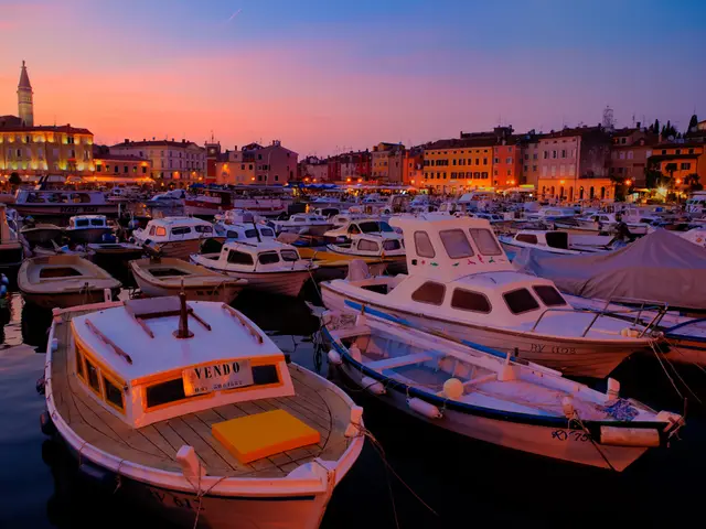 In this image there are ships in the water. At the background there are buildings, towers and sky.