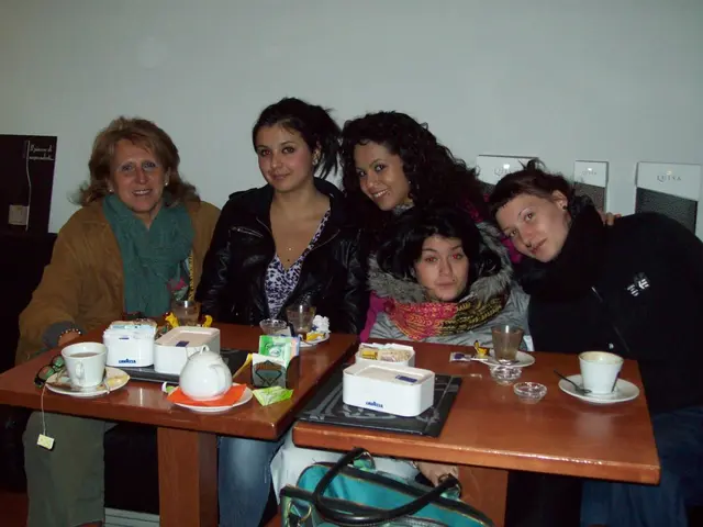 This picture is a group of five ladies smiling and have a table in front of them with some coffee...