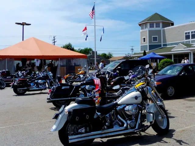 In this image there are some bikes and cars parked in a parking lot and there is a tent, behind the...