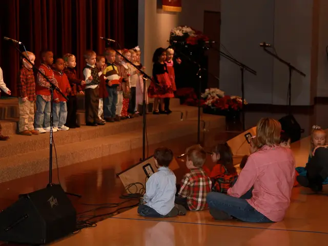 This image consists of many children on the dais. And there are mics along with mic stands. At the...