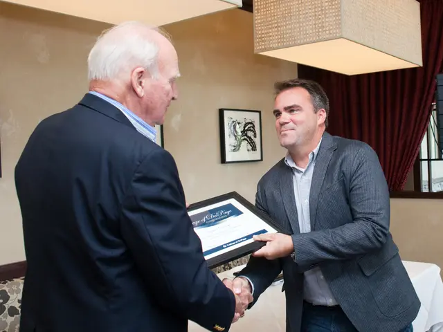 In the picture I can see two men are standing and giving handshake to each other. The man on the...