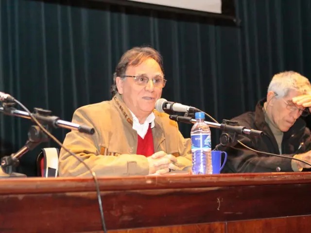 There are two men sitting and wearing specs. In front of them there is a platform. On that there...