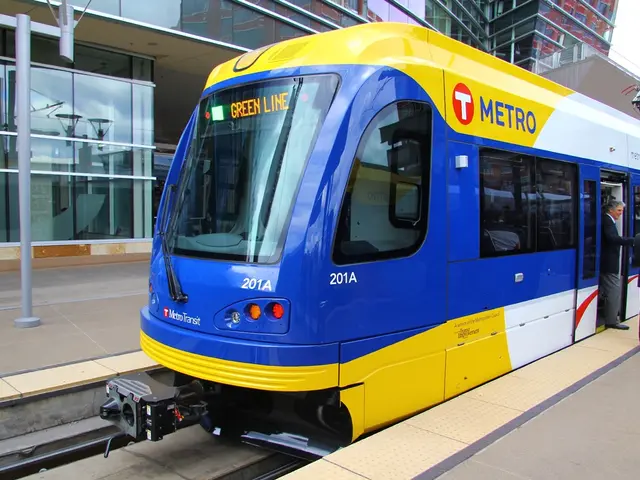 There is a train on a railway track. 2 men are standing wearing suit. There are glass buildings at...