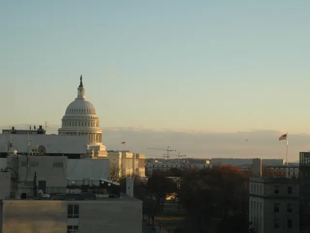 In this image there are buildings, trees, flags and sky. At the bottom of the image there is a...