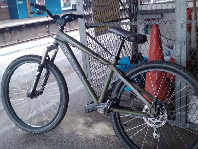 In this image we can see bicycle which is of green color and in the background there is fencing,...