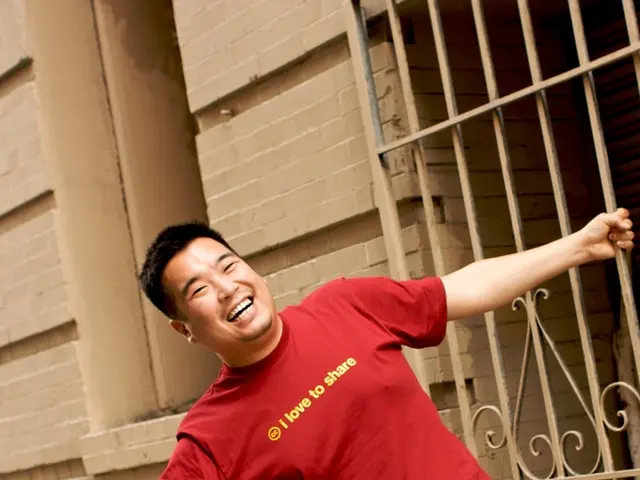 In this image we can see a person wearing red color T-shirt, blue color jeans standing, smiling by...