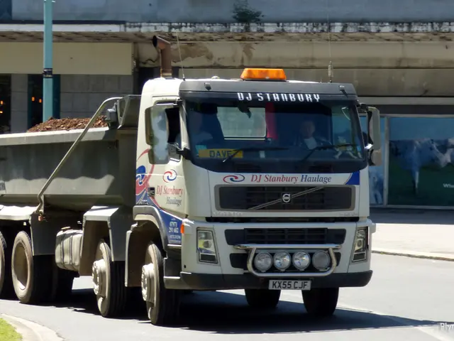 In this image a truck is moving on the road. in the background there are buildings. Here there is a...