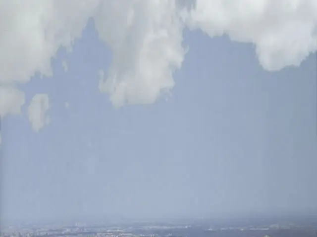 In this picture I can see the city. At the bottom I can see the skyscrapers, buildings and sheds....