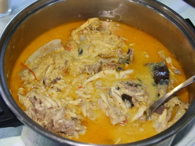 In the image there is a bowl with meat soup and spoon in it on a table.