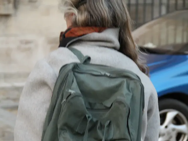 As we can see in the image, there is a woman wearing bag and on road there is a car.