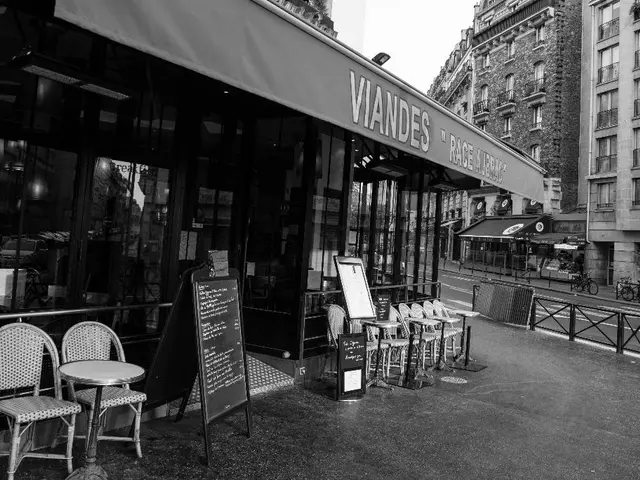 This is a black and white image. At the center of the image there is a store,There are chairs. At...