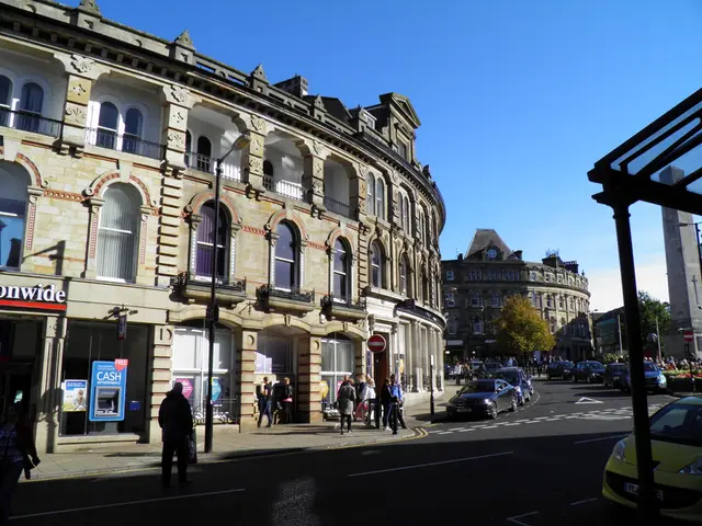 This is the picture of city. In this image there are group of people standing on the footpath and...