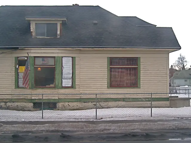 There is a fencing near snow surface on the ground. In the background, there is a house which is...