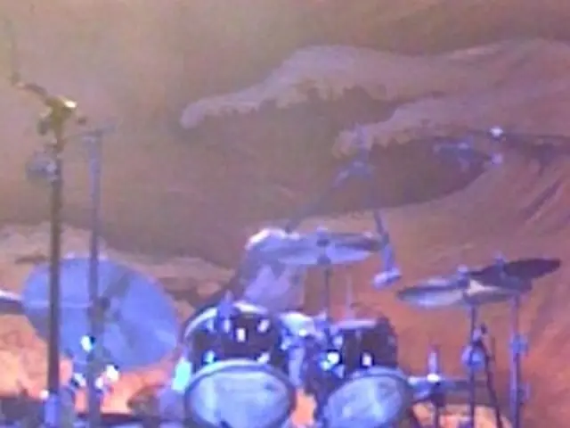 In the image there are many drugs and behind the drums a person is sitting.