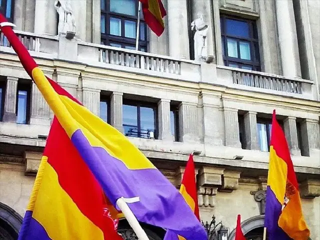 There is a building it has a lot of windows and doors, there are some flags stick to the poles in...