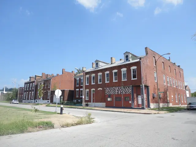 In this image in the center there is a building and poles, street lights, trees and some vehicles...