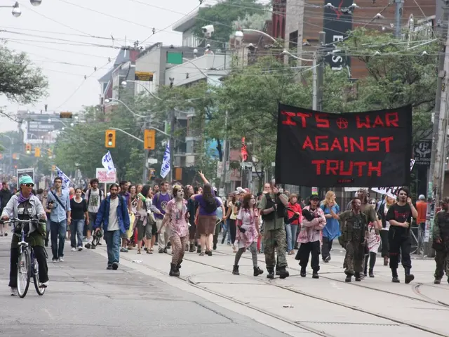 In this image there are a few people holding flags, banners are marching down the road and there is...