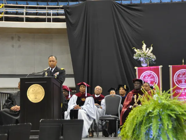 In this picture we can see a plant in the front, there are some people sitting on chairs and a man...
