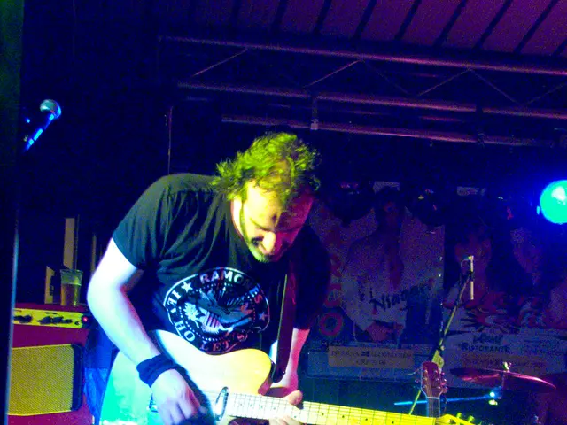 This is a picture of a man who is wearing a black shirt and holding a guitar and there is a black...