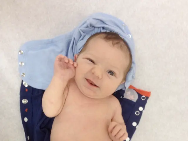 In the image there is a baby and under the baby there are two clothes.