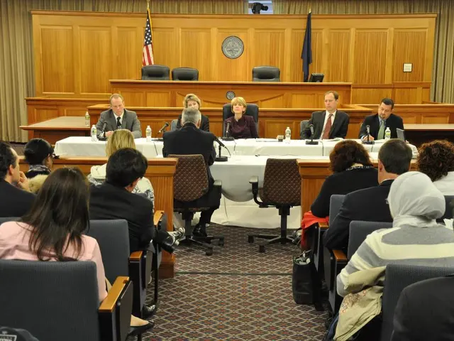 This is a meeting hall where we can see a group of people sitting on chairs and also two flags of...