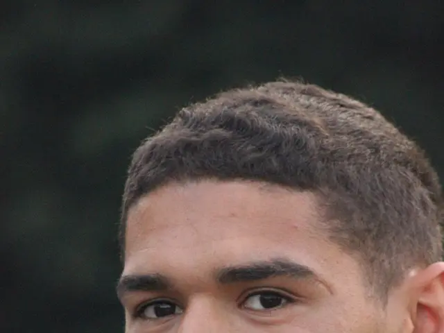 In the image there is a man smiling. Behind him there is a blur background.