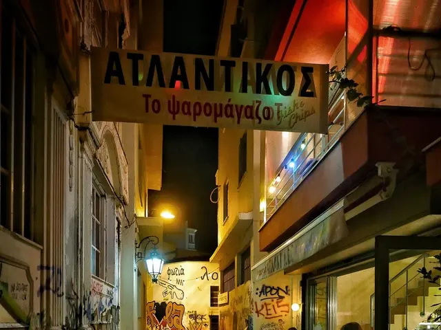 In this image I can see few people are standing and few people are sitting on the chairs. On the...