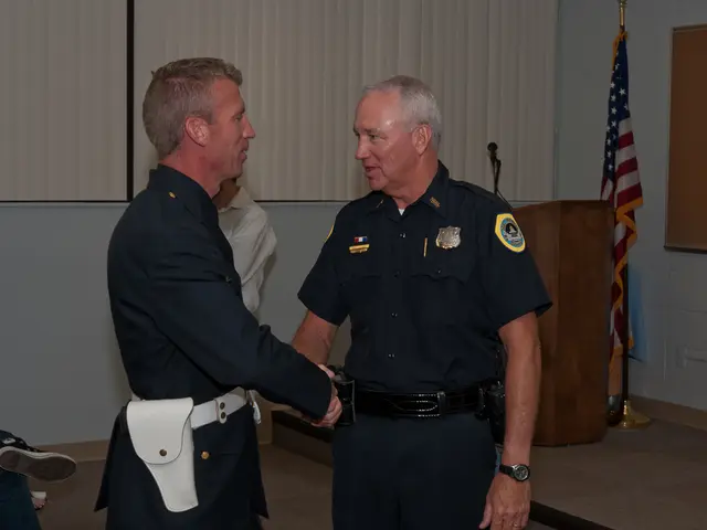 In this picture I can see 2 men in front and I see they're shaking hands and I see they're wearing...