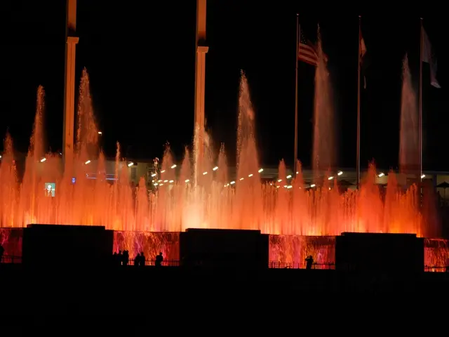 In this picture I can see the flags. I can see the fountain. I can see a few people standing on the...