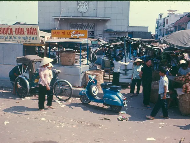 The picture is taken on the street of a city. In the center of the picture there are shops, tents,...