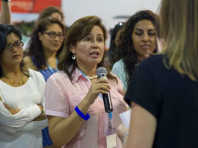 In this image a group of women facing towards the right among which one woman in the center is...
