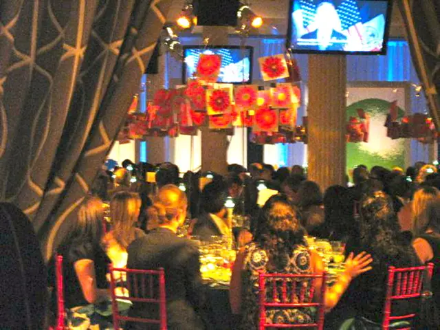 This pictures looks like a party. We see few people seated on the chairs and we see tables with...