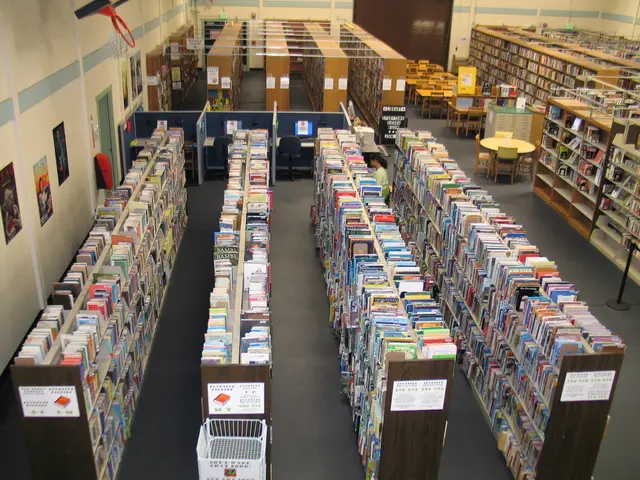 In this image, we can see library. There are racks contains some books. There are tables and chairs...