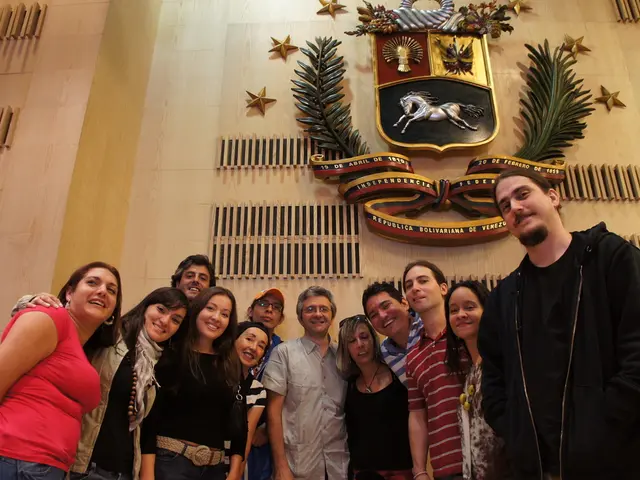 In the image there are many men and women standing in front of the wall with a symbol,plants and...