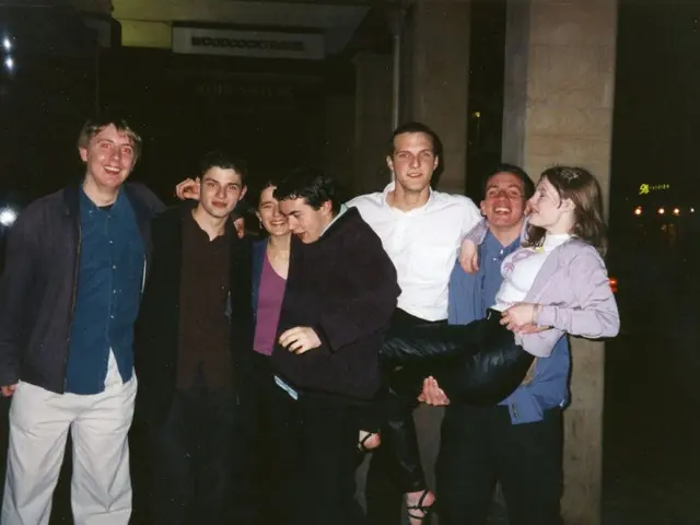 In this image I can see few persons standing and there is a man carrying a woman. There are pillars...