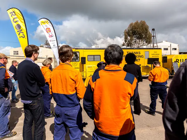 In this image there are people standing, in the background there are vehicles, houses, trees and...