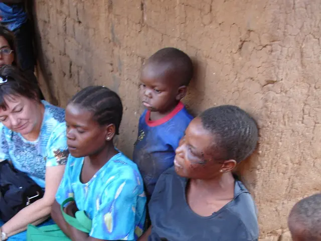 In this image we can see women and children standing and sitting on the ground.