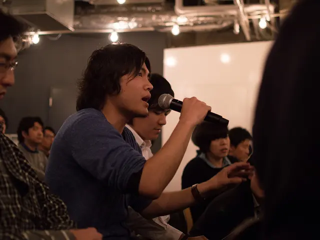 This picture describe a group of people sitting in the hall and in front a boy wearing blue sleeves...