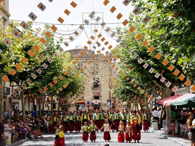 Here we can see crowd and this is a road. There are flags, trees, umbrellas, boards, and buildings....
