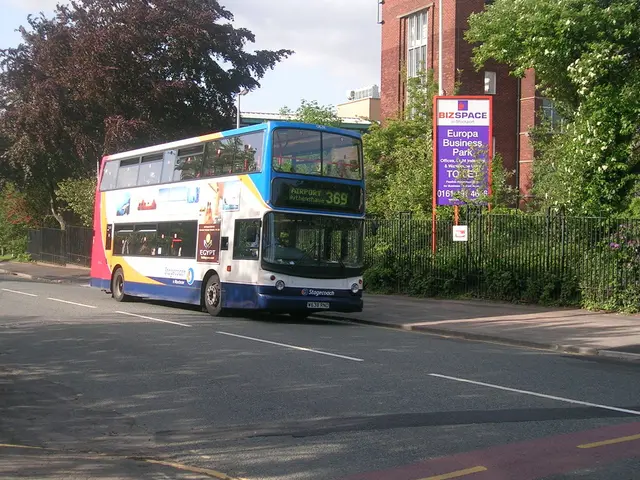 In this image there is a bus on the road. Behind the bus there is a metal fence. There is a board....