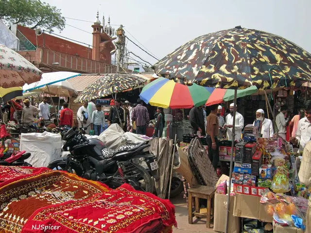 The picture consists of umbrellas, vehicles, mats, boxes, stool, people and many other objects. In...